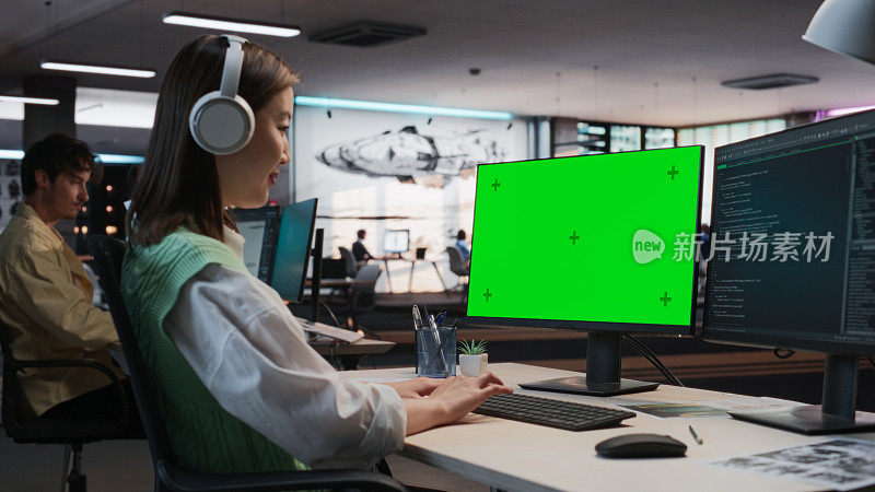 亚洲女性游戏程序员在游戏开发工作室办公室用绿屏Chromakey在台式电脑上编程。专注女性为新3D RPG电子游戏设计游戏玩法